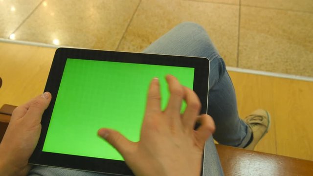 Young girl sitting at bench in shopping mall and working with tablet. Female hands using tablet pc with green screen. Chroma key