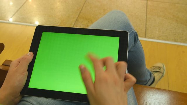 Young girl sitting at bench in shopping mall and working with tablet. Female hands using tablet pc with green screen. Chroma key
