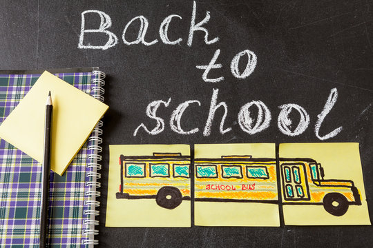 Back to school background with title "Back to school"  written by white chalk on the black chalkboard and the picture of school bus drawn on yellow pieces of paper and notebook with pencil