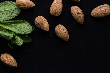 Almonds in shell with mint leaves on black background with copy space closeup. Top view
