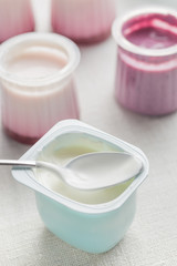 Obraz na płótnie Canvas Yogurts assortment in plastic bowls on light cloth background. Natural and fruit healthy, diet, gourmet dessert for granola breakfast. Sweet yoghurts closeup.