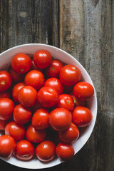 Cherry tomatoes covered with water drops in white bowl on rustic wooden backdrop. Top view, selective focus, toned image