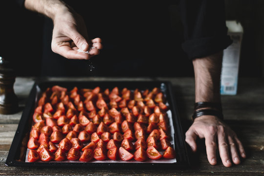 Male chef salting down tomatoes on a tray. Preparing cherry tomatoes for roasting