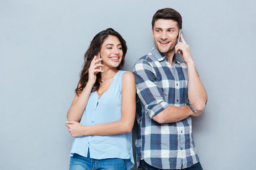 Smiling couple using mobile phones over gray background