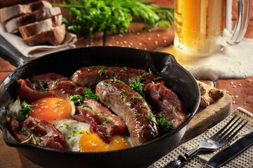 Male brutal dinner of fried sausages, bacon, scrambled eggs on the background of beer, herbs and...
