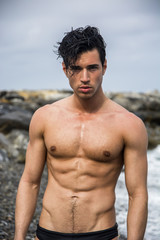 Young shirtless athletic man standing in water by ocean shore