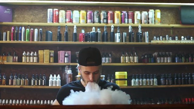 vape shop seller show e-cigarettes to buyer and exhaling smoke