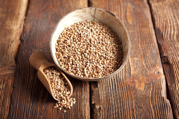 Buckwheat in scoop and bowl on wooden table