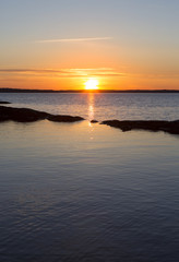 Obraz premium Sun is going down far away on a peaceful night. Some stones are like small island in the front. Glowing sky is colorful in the evening in Finland.