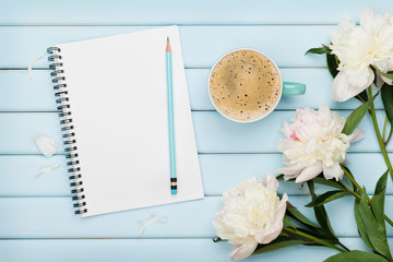 Morning coffee mug, empty notebook, pencil and white peony flowers on blue wooden table, cozy...