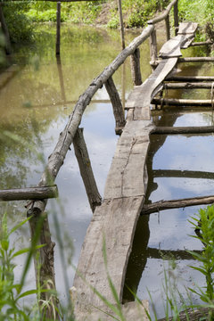 Old wooden bridge over the lake overgrown with grass. Old rural landscape.