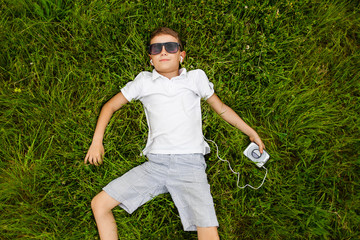 Little boy with retro media player listening to music outdoor on the grass. Kid taking relax with music. Green summer garden.