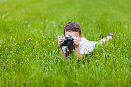 Little boy with retro photo camera shooting outdoor. Kid taking a photo using a film cam. Green summer garden. Young photographer.