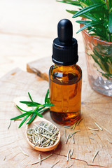 a bottle of rosemary aromatherapy oil extract with fresh and dried rosemary leaf on wooden spoon.