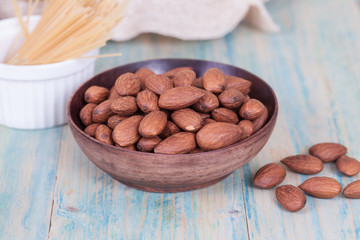 Almonds in brown bowl on textured wooden background
