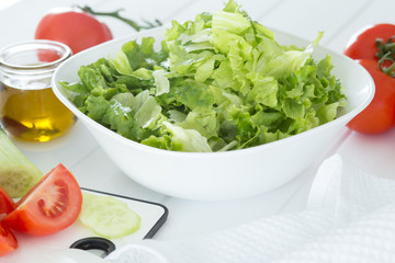 Preparing a healthy fresh salad with tomato, lettuce, cucumber and oil