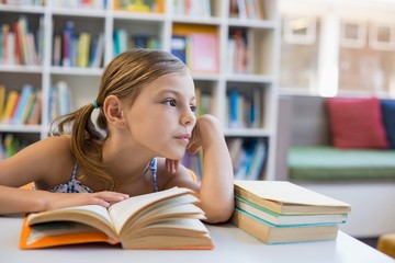 Thoughtful school girl reading book in library