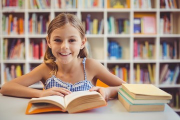 Smiling school girl reading a book in library