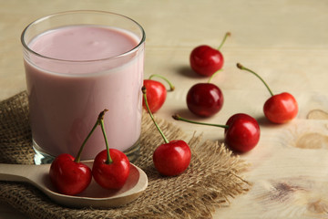 yogurt with cherry flavor in a Cup on burlap on wooden background with wooden spoon