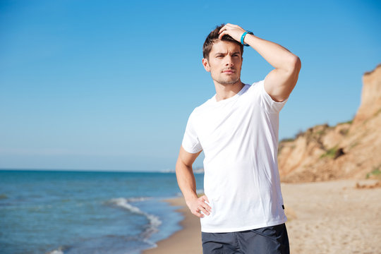 Attractive young man standing and thinking on the beach