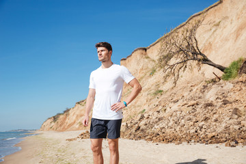 Thoughtful attractive young man standing on the beach and thinking