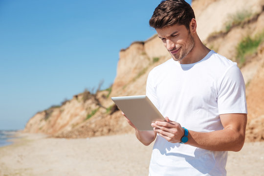 Happy young man using tablet on the beach