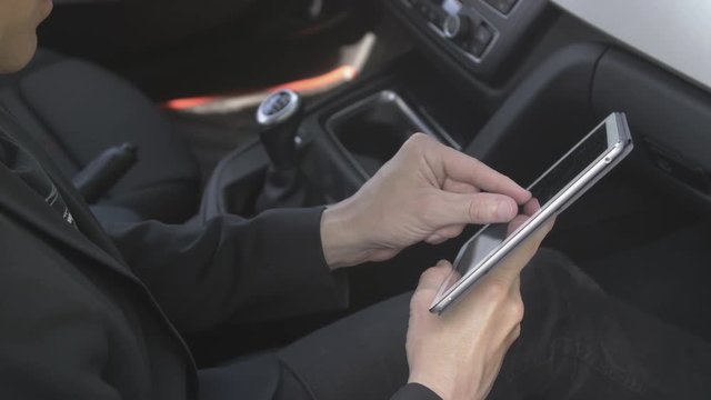 Caucasian man browsing and using gestures on a tablet computer in the passenger seat in a car. For concepts such as sms, text messaging, chat and web browsing.
