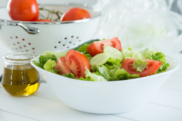 Preparing a healthy fresh salad with tomato, lettuce, cucumber and oil