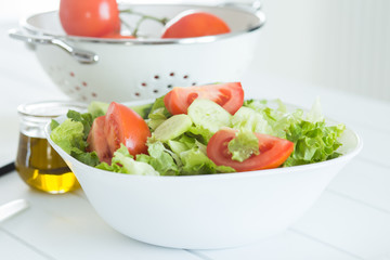 Preparing a healthy fresh salad with tomato, lettuce, cucumber and oil

