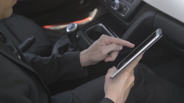 Caucasian man typing mail on a tablet computer in the passenger seat in a car. For concepts such as sms, text messaging, chat and web browsing.