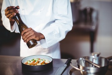 Mid section of chef sprinkling pepper on a meal