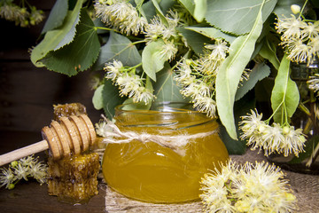 Jar with honey, honeycomb with pollen and linden flowers on a dark wooden background