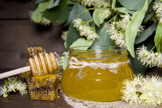 Jar with honey, honeycomb with pollen and linden flowers on a dark wooden background