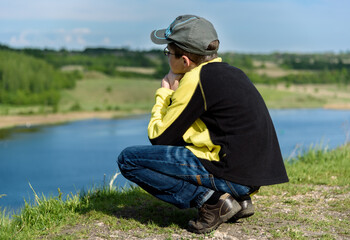Naklejka na ściany i meble lonely boy teenager sits on a hill above lake