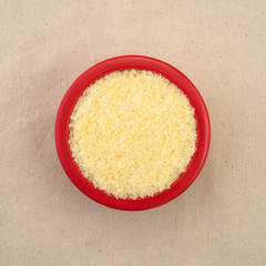 Small bowl of grated Pecorino Romano cheese on a beige tablecloth top view.