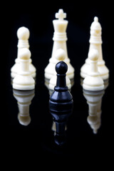 black pawn in front of white chess pieces on a black background with reflection