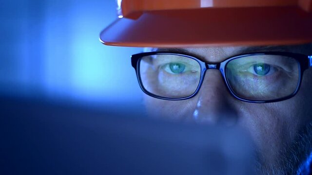 Blue ambiance, a engineer with a security helmet  working on a laptop. 