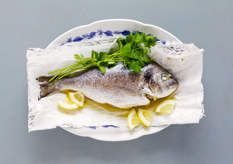 fried fish , lemon and fresh parsley. on grey table
