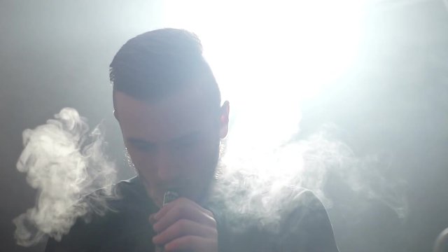 young vaper man exhaling big clouds of smoke with e-cigarette vape in slowmotion