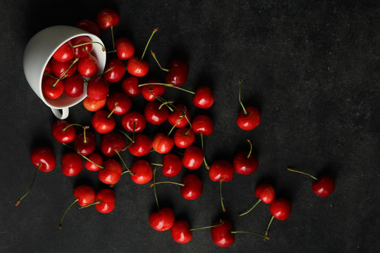 heap of sweet cherries in a Cup and scattered on a black background
