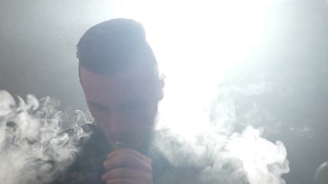 young vaper man exhaling big clouds of smoke with e-cigarette vape in slowmotion