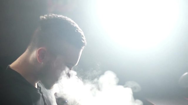 young vaper man exhaling big clouds of smoke with e-cigarette vape in slowmotion