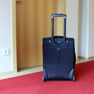 schwarzer Koffer mit Rollen im Hotel