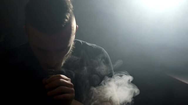 young vaper man exhaling big clouds of smoke with e-cigarette vape in slowmotion