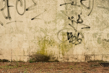 Hintergrund – Schmutzige Wand mit Graffit Schmierereien und Ascheplatz mit Unkraut als Boden