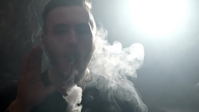young vaper man exhaling big clouds of smoke with e-cigarette vape in slowmotion