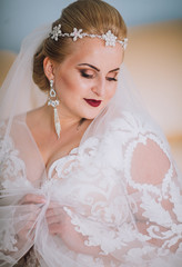 Fototapeta na wymiar Portrait of beautiful woman in white dress. Bride with crown and wears earrings. Amazing make up.