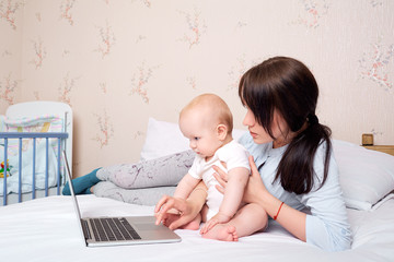 Mother with baby on the bed looking at a laptop with enthusiasm