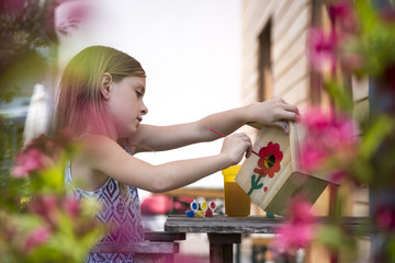Girl painting red flower on a birdhouse