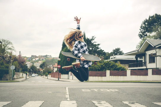 Carefree young woman with skateboard jumping on the street